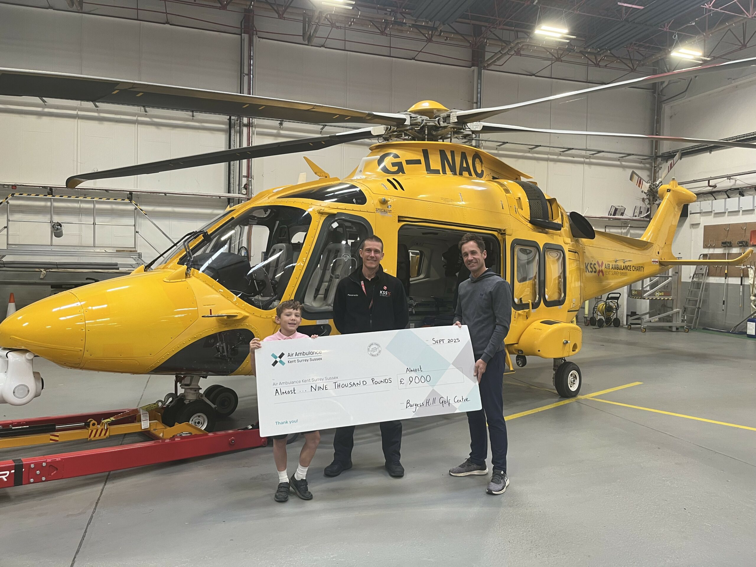 Burgess Hill Golf Centre cheque presentation beside the KSS air ambulance during a 2025 visit
